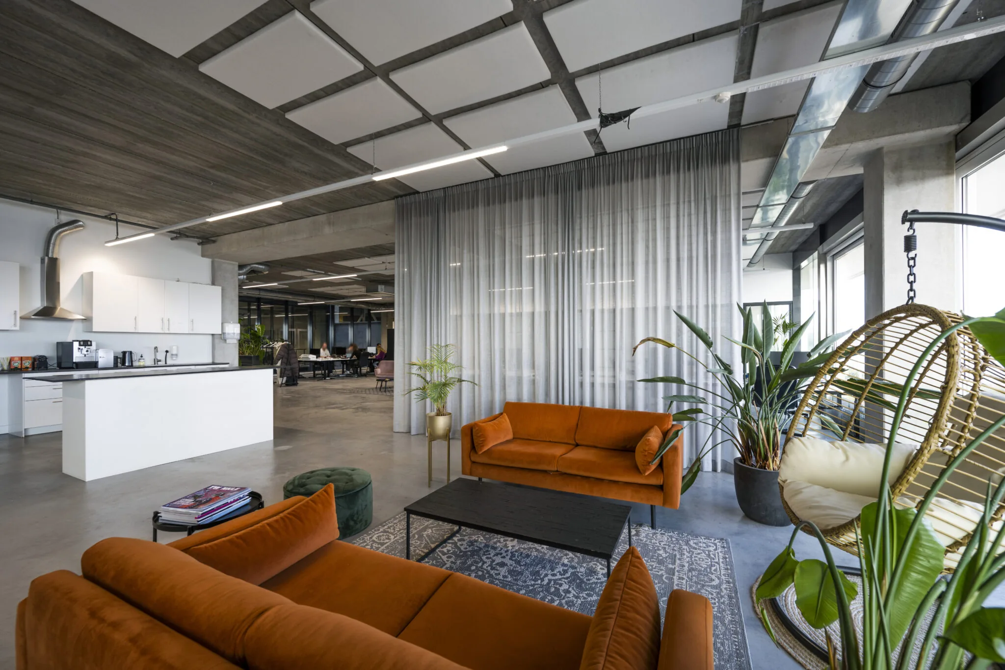 Moderne kantoorruimte aan de Danzigerkade met oranje banken, planten, open keuken en een hangstoel.