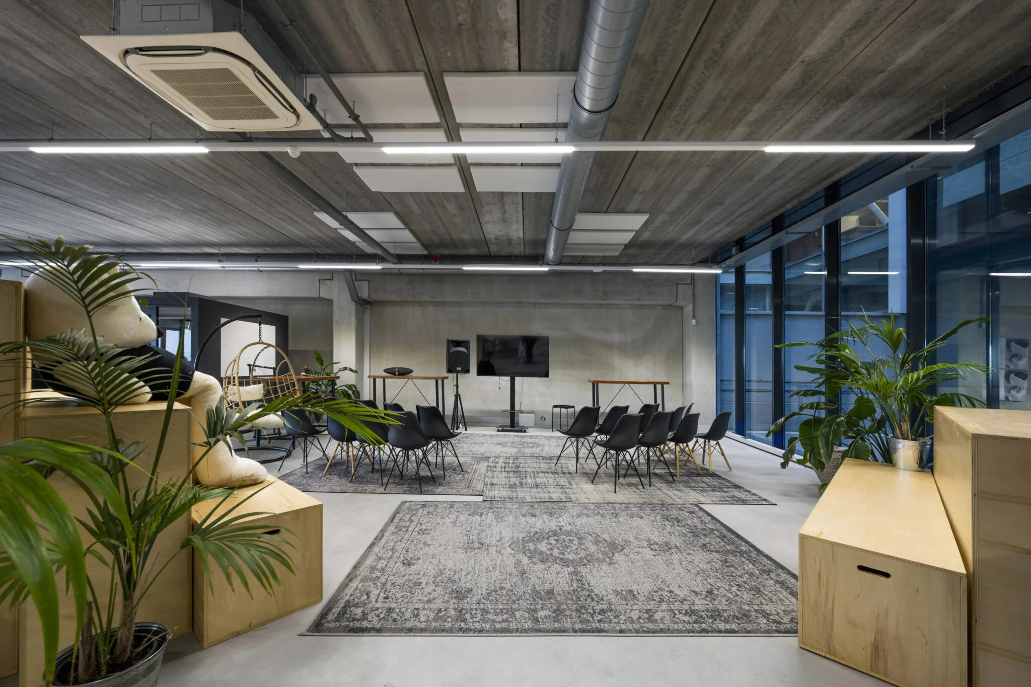 Moderne, industrieel ingerichte vergaderruimte aan de Danzigerkade met zwarte stoelen, planten en een groot beeldscherm.