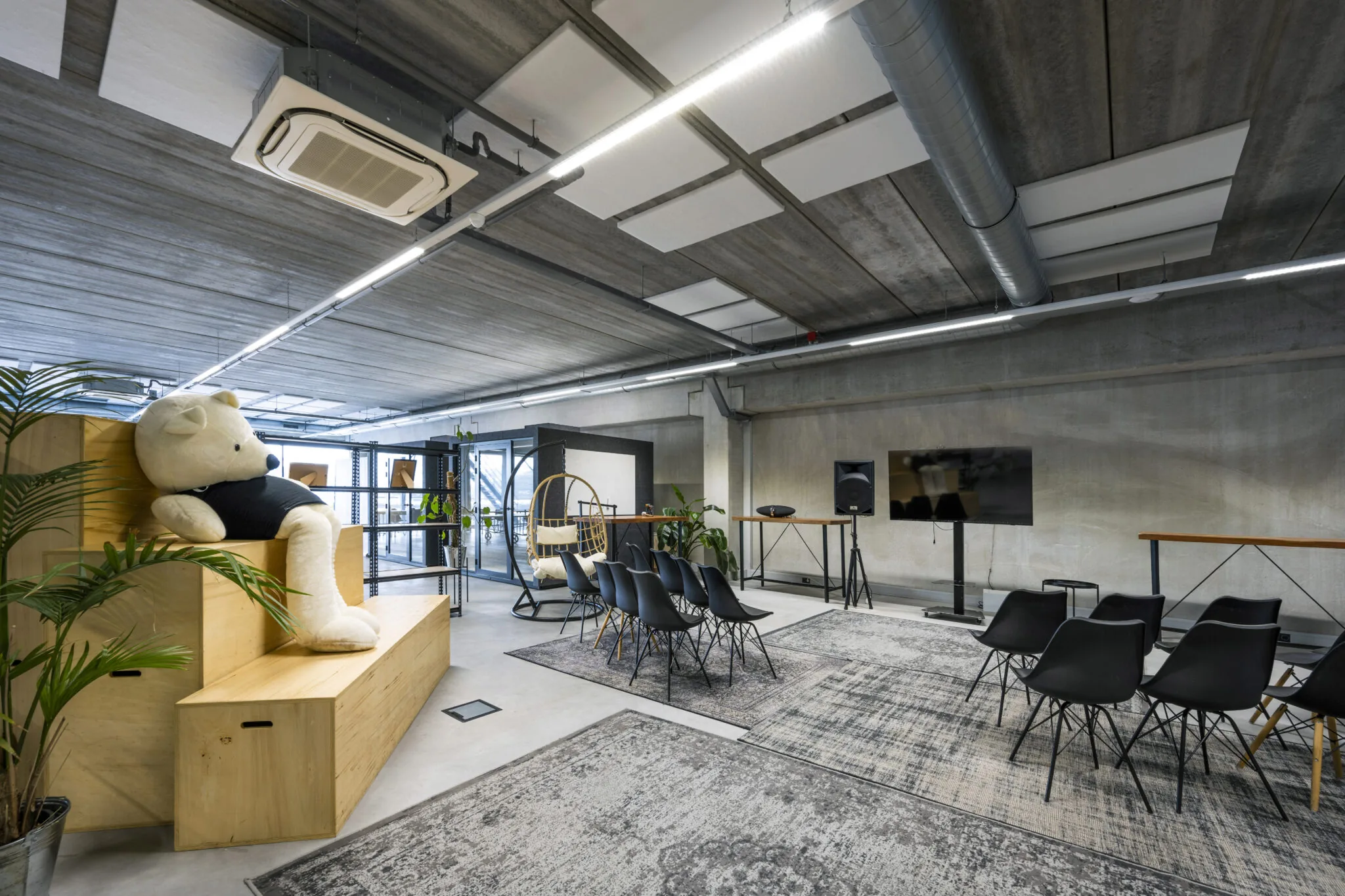 Moderne kantoorruimte aan de Danzigerkade met zitplekken, een grote teddybeer op houten tribune-elementen en een presentatiescherm.