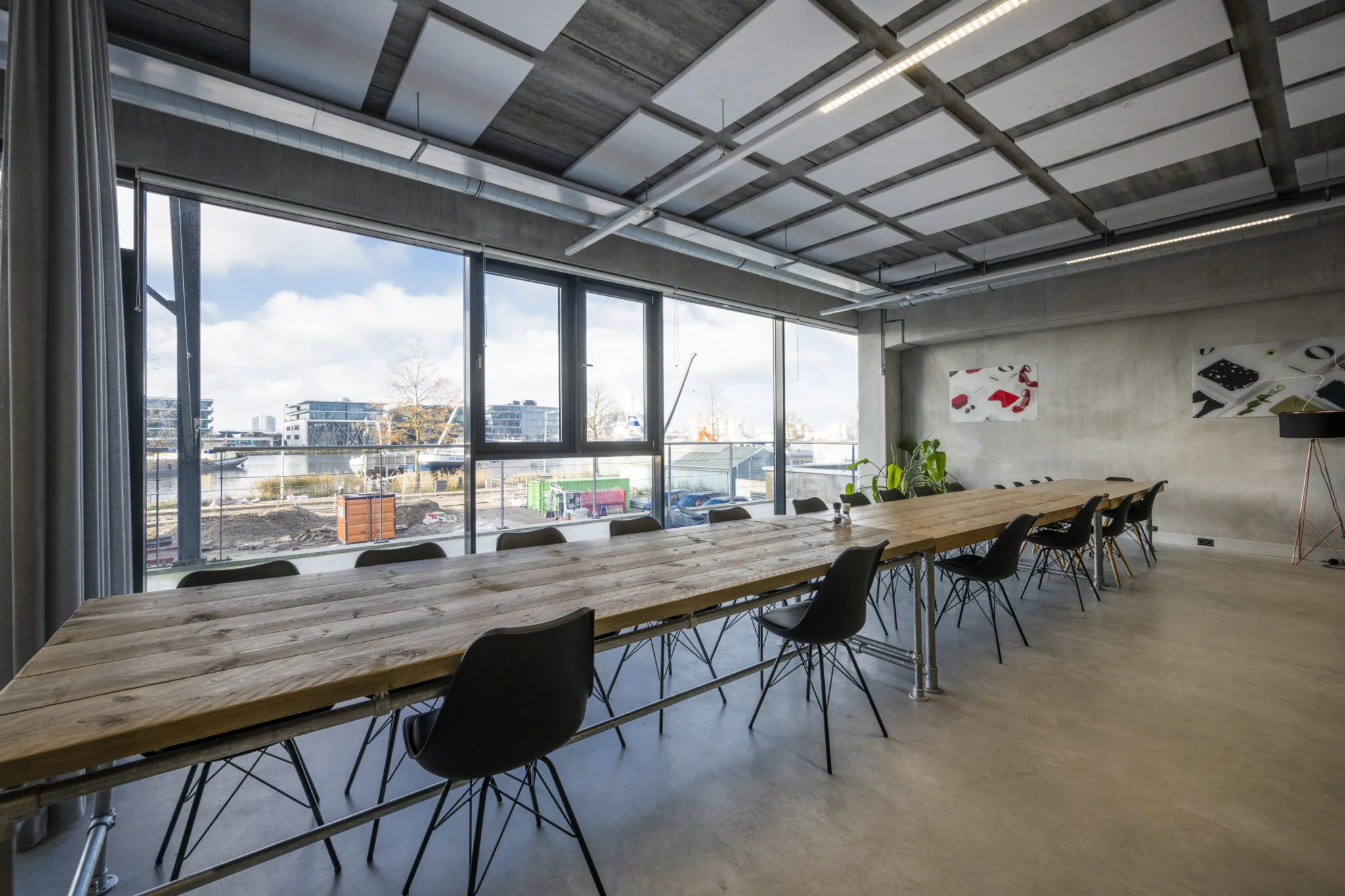 Vergaderruimte aan de Danzigerkade met een lange houten tafel, zwarte stoelen en uitzicht op moderne bebouwing en een bouwplaats.