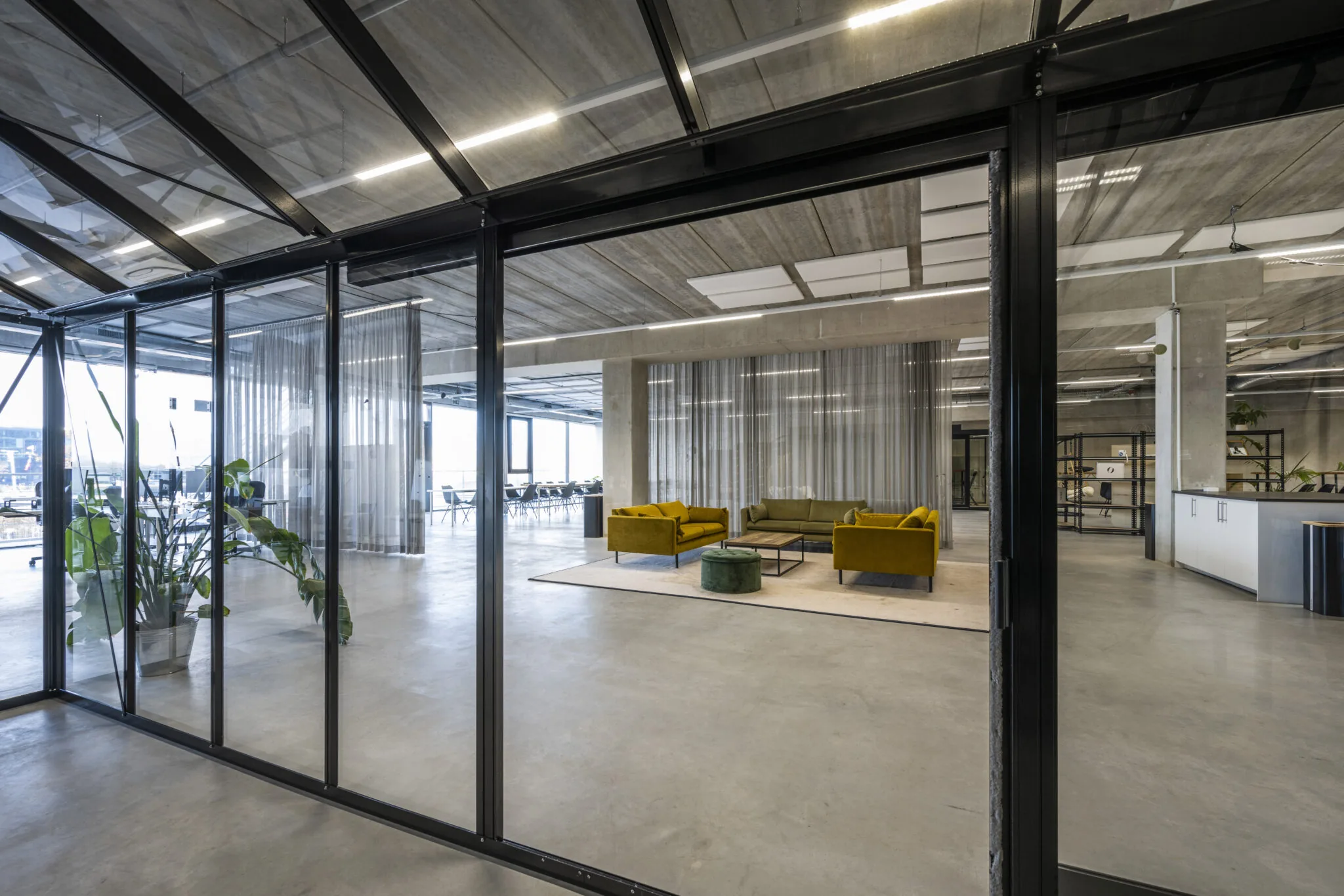 Moderne kantoorruimte aan de Danzigerkade met glazen wanden, betonnen plafond en een zithoek met kleurrijke banken.