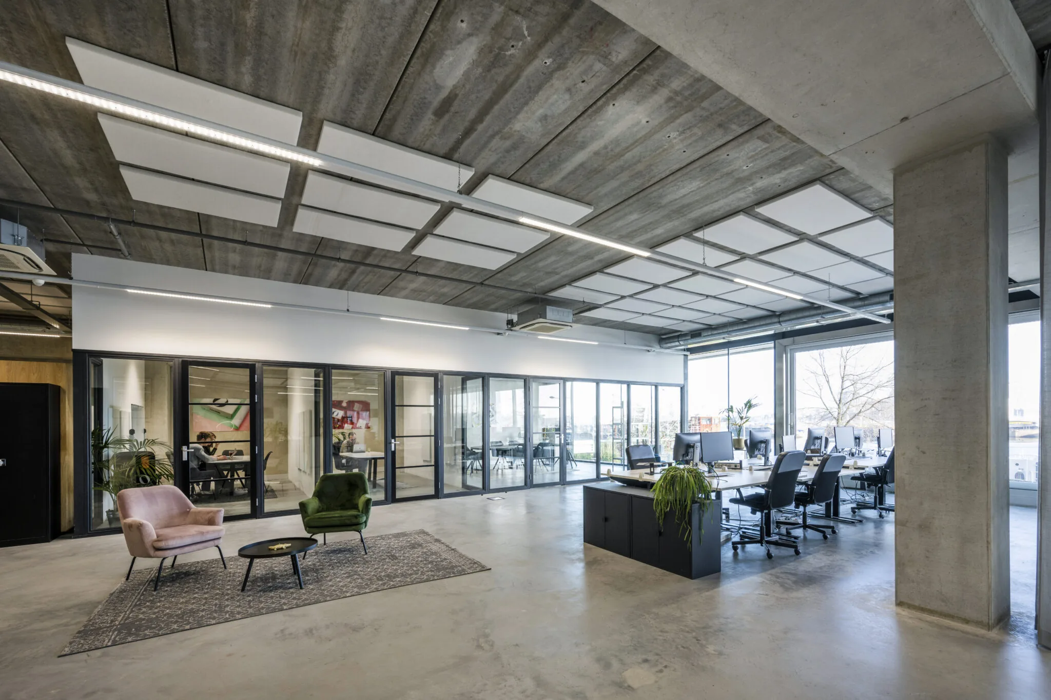 Modern kantoorinterieur aan de Danzigerkade met open werkplekken, glazen vergaderruimtes en een zithoek met kleurrijke stoelen.