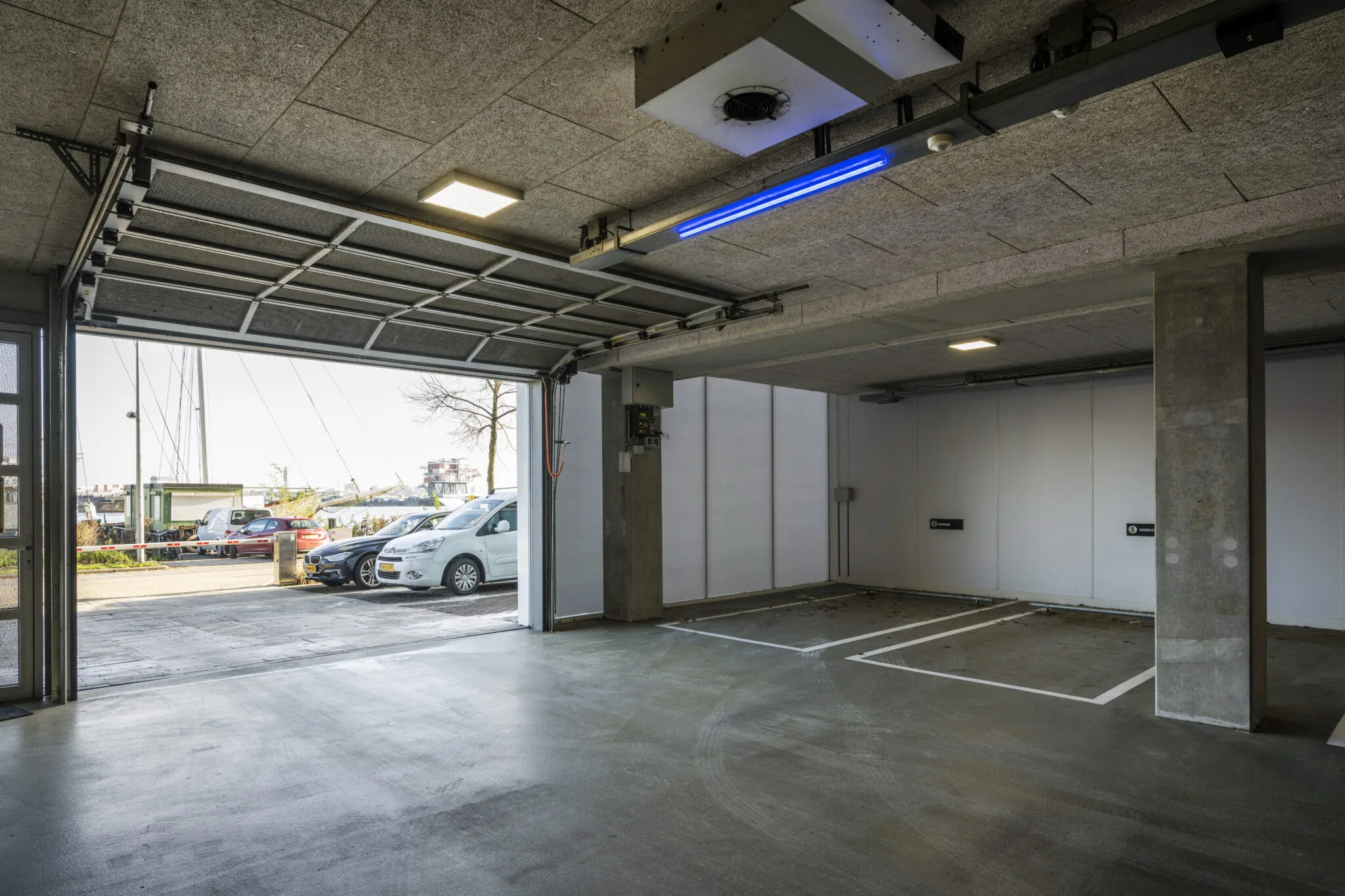 Openstaande garagedeur aan de Danzigerkade met zicht op lege parkeerplaatsen en geparkeerde auto's buiten.