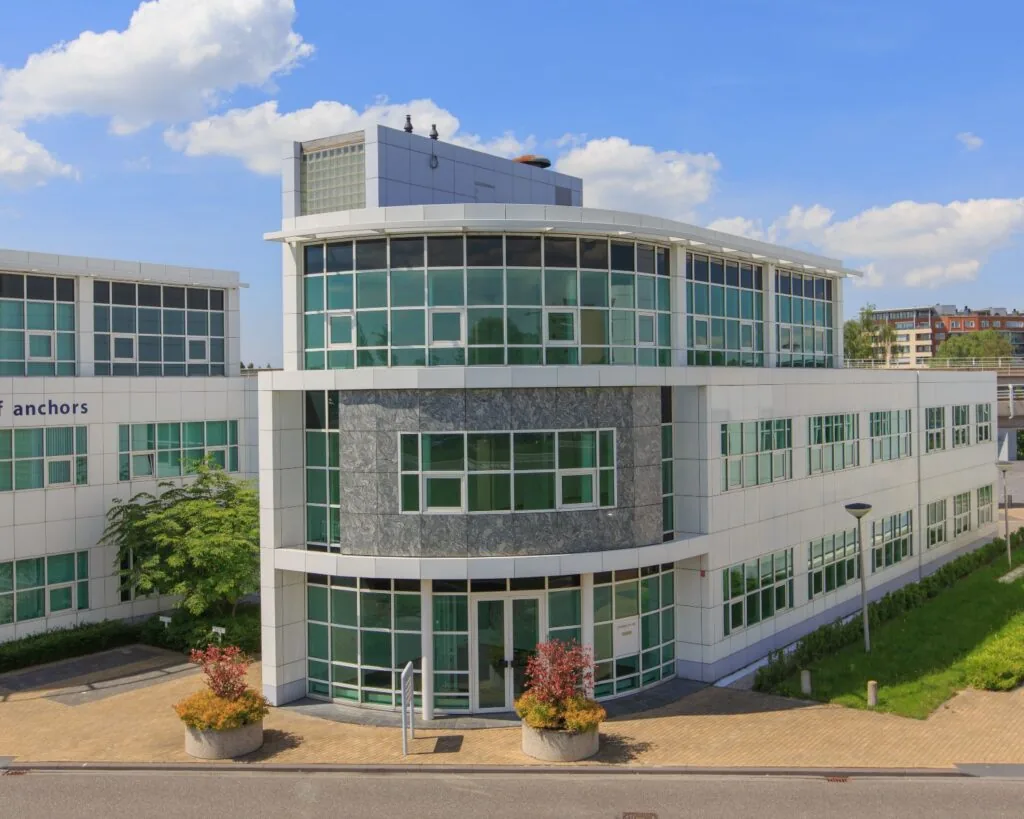 Modern kantoorgebouw met veel glas en witte gevelpanelen, gefotografeerd op een zonnige dag.