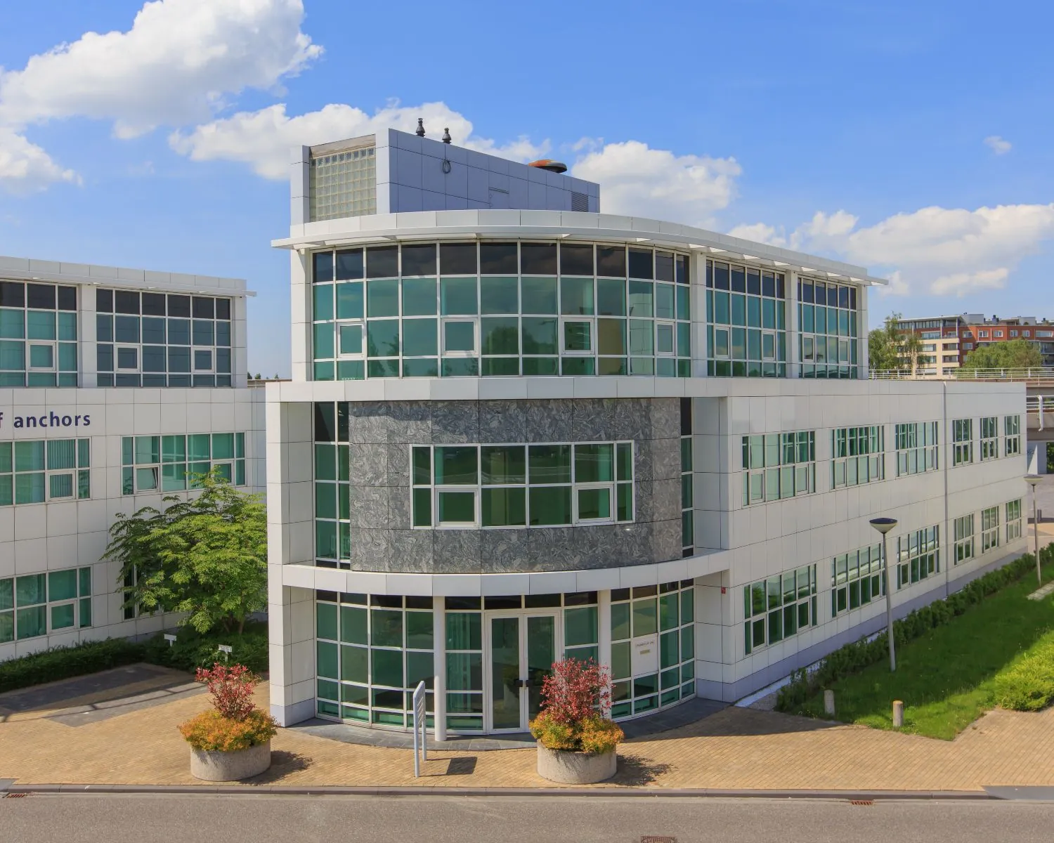 Modern kantoorgebouw met veel glas en witte gevelpanelen, gefotografeerd op een zonnige dag.