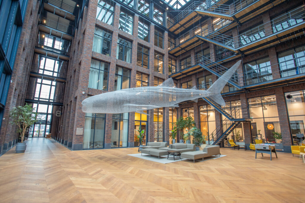 Een grote, doorzichtige sculptuur van een haai hangt in het atrium van een modern kantoorgebouw.