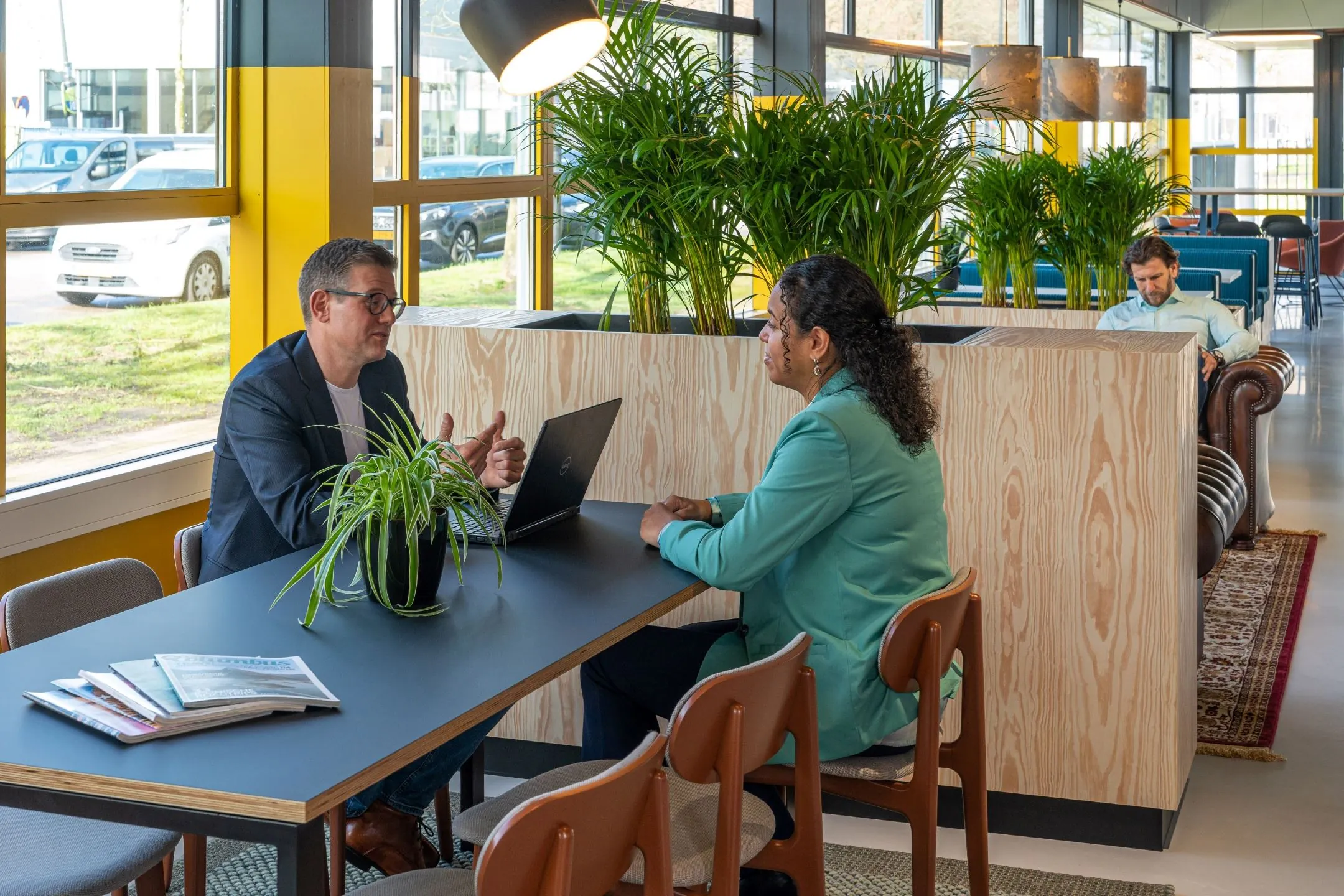 Twee mensen voeren een gesprek aan een tafel met een laptop in een modern kantoor aan de Disketteweg 14.