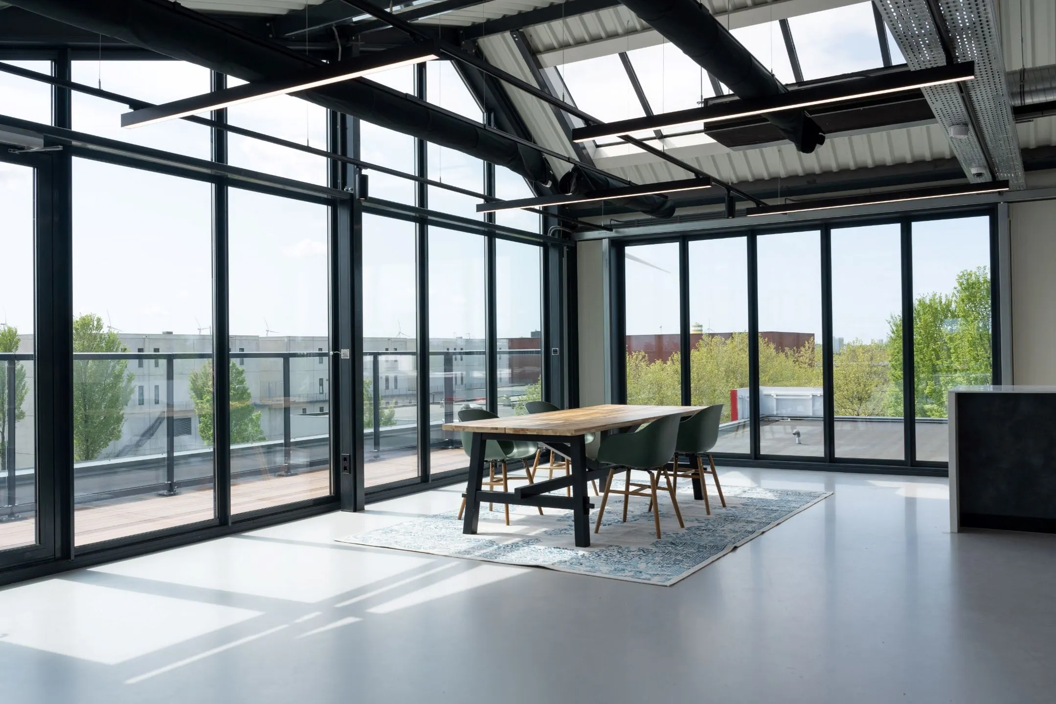 Vergaderruimte op Disketteweg 14 met een houten tafel, zes stoelen en grote ramen met uitzicht op een dakterras en groen.