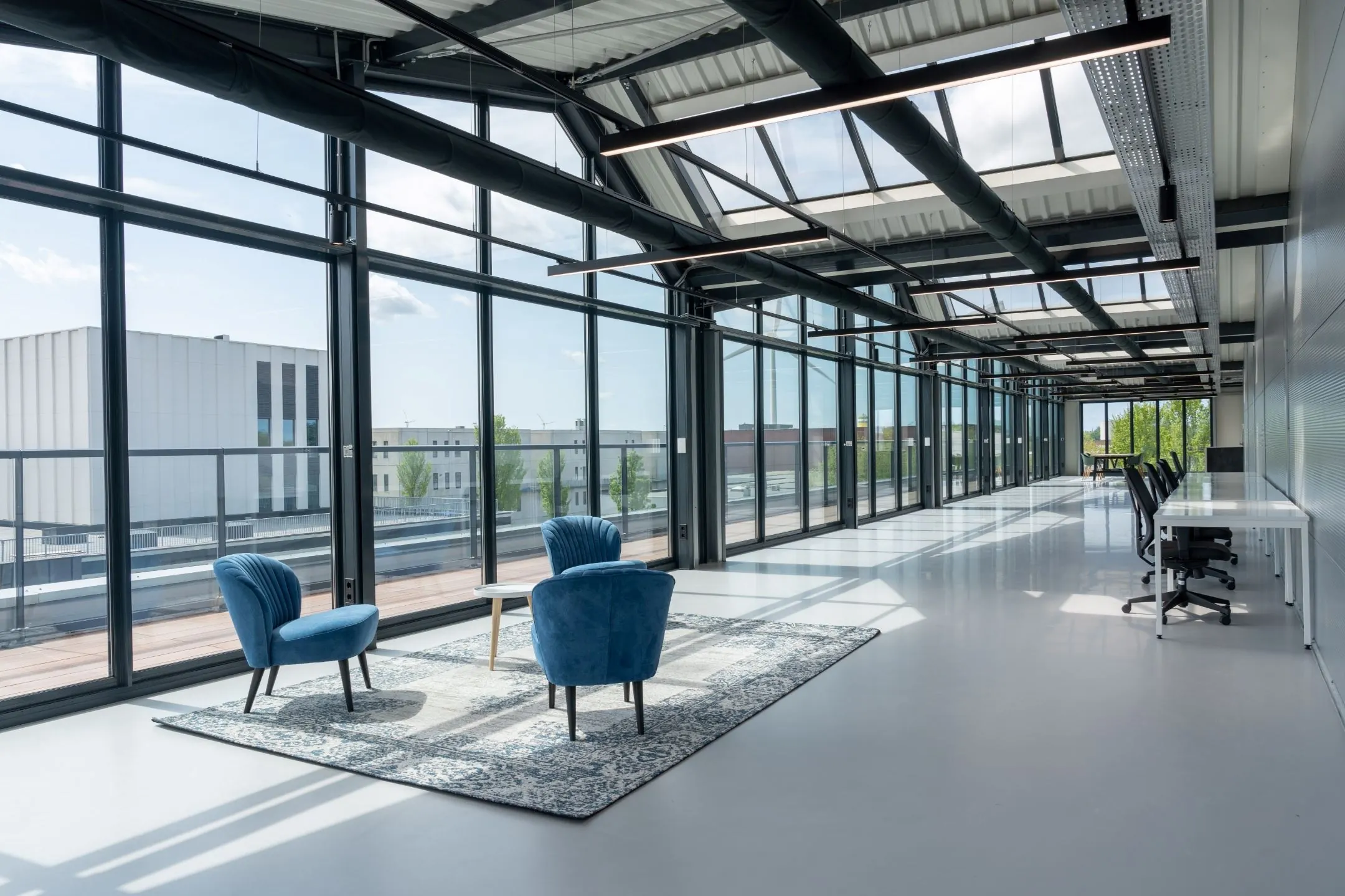 Lichte en moderne kantoorruimte aan de Disketteweg met glazen wanden, blauwe fauteuils en werkplekken langs de zijkant.