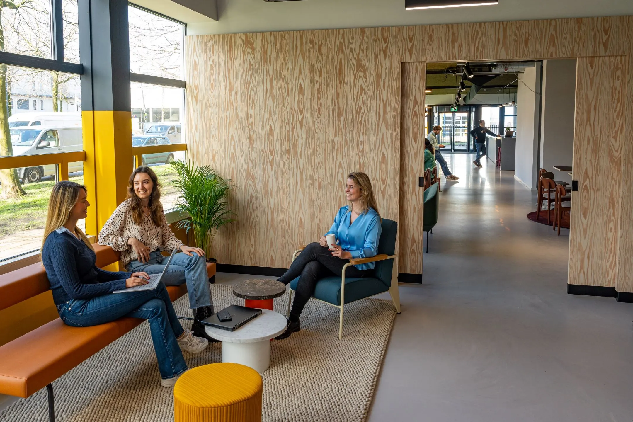 Drie vrouwen zitten in een moderne loungeruimte op Disketteweg 14 terwijl ze met elkaar in gesprek zijn.