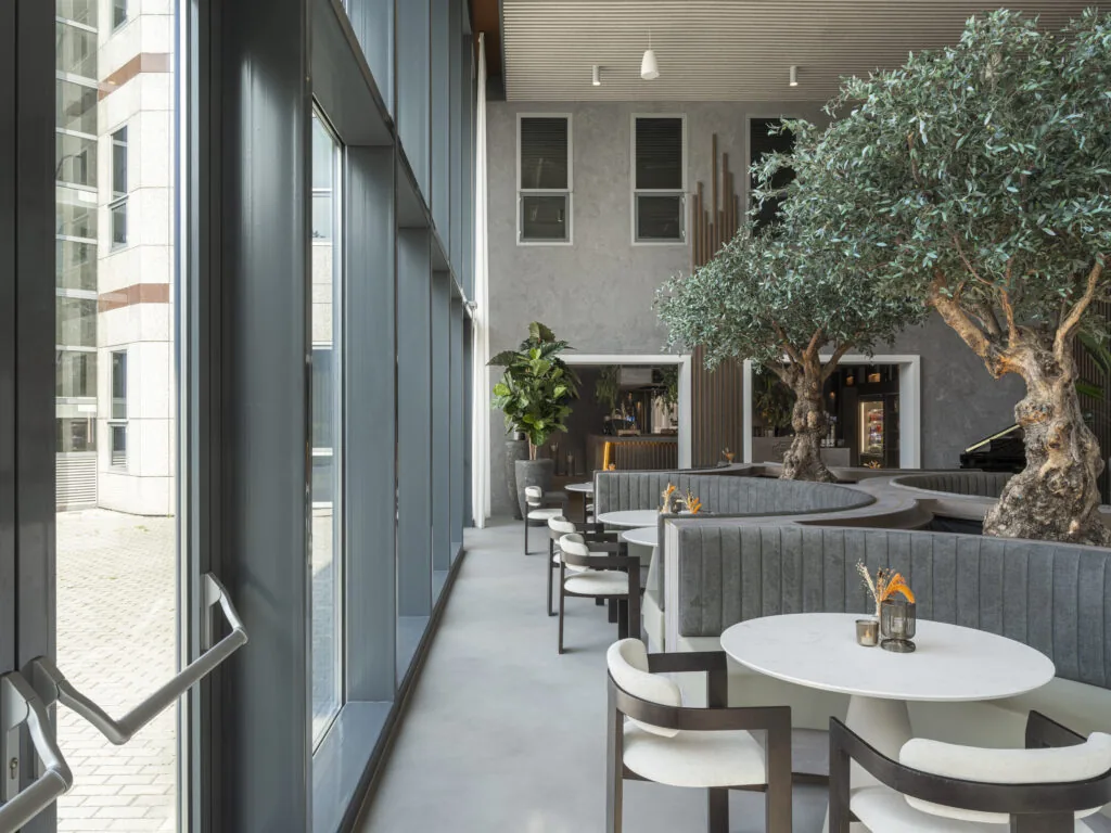 Moderne kantoorlounge in Tower 42 met ronde zitbanken, grote ramen en olijfbomen als interieuraccent.