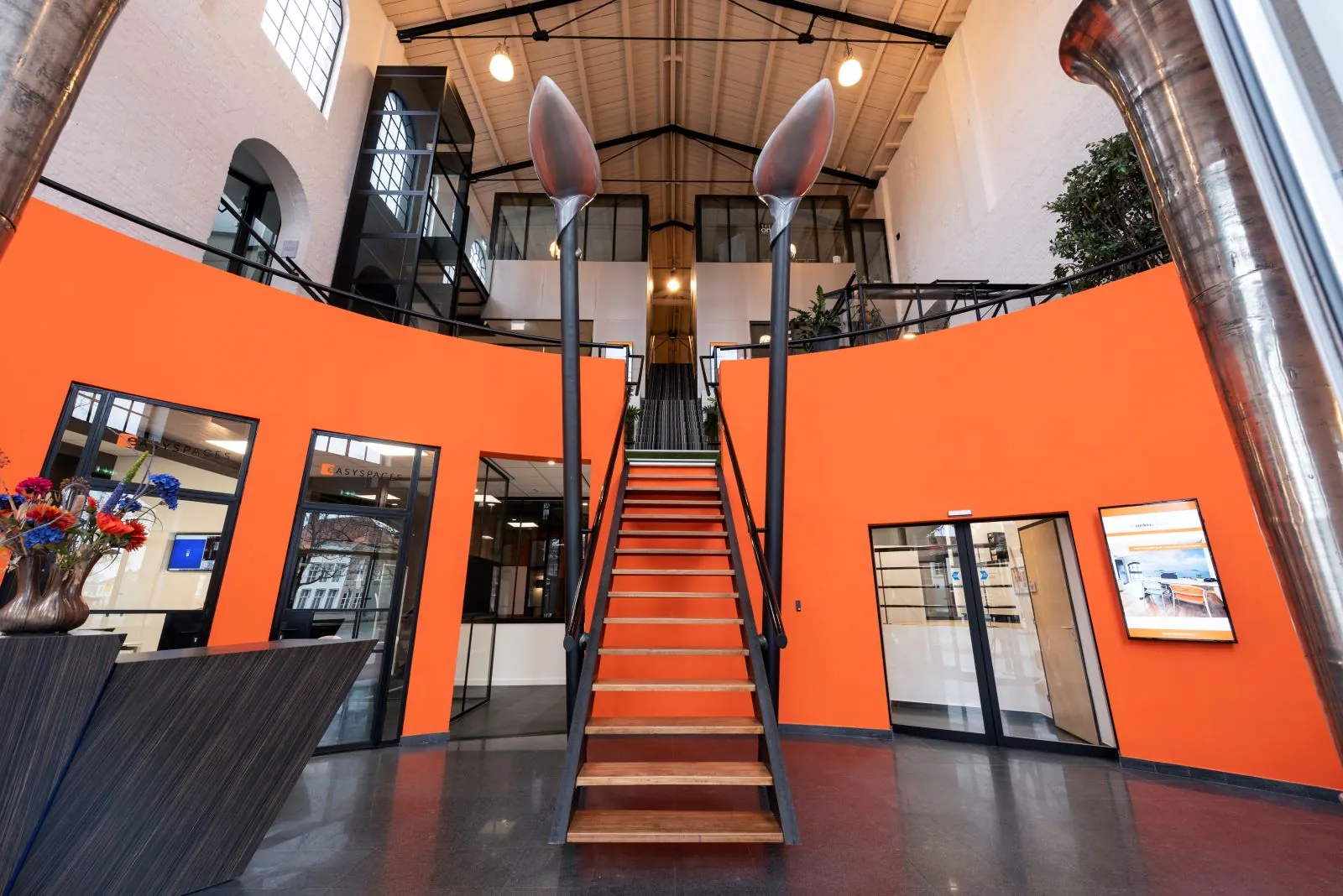 Entree van het Suiker-gebouw met een opvallende oranje muur, centrale trap en twee grote lepels als kunstobject.