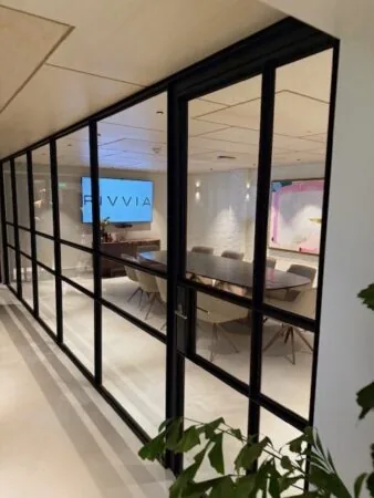 Vergaderruimte met glazen wanden, een groot scherm met het logo “RIVVIA” en een lange vergadertafel met stoelen.