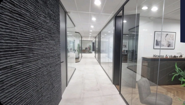Moderne kantoorruimte met glazen wanden, een zwarte structuurwand en het logo van Kroes & Visser bij de receptie.