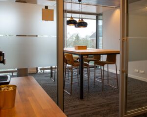 Moderne vergaderruimte met hoge houten tafel, barkrukken en hanglampen bij een glazen wand.