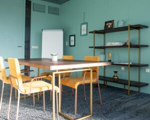Vergaderruimte met turquoise muren, een houten tafel, gele stoelen en een flip-over.
