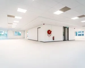 Licht en modern leeg kantoorpand met witte wanden, systeemplafond en grote ramen.