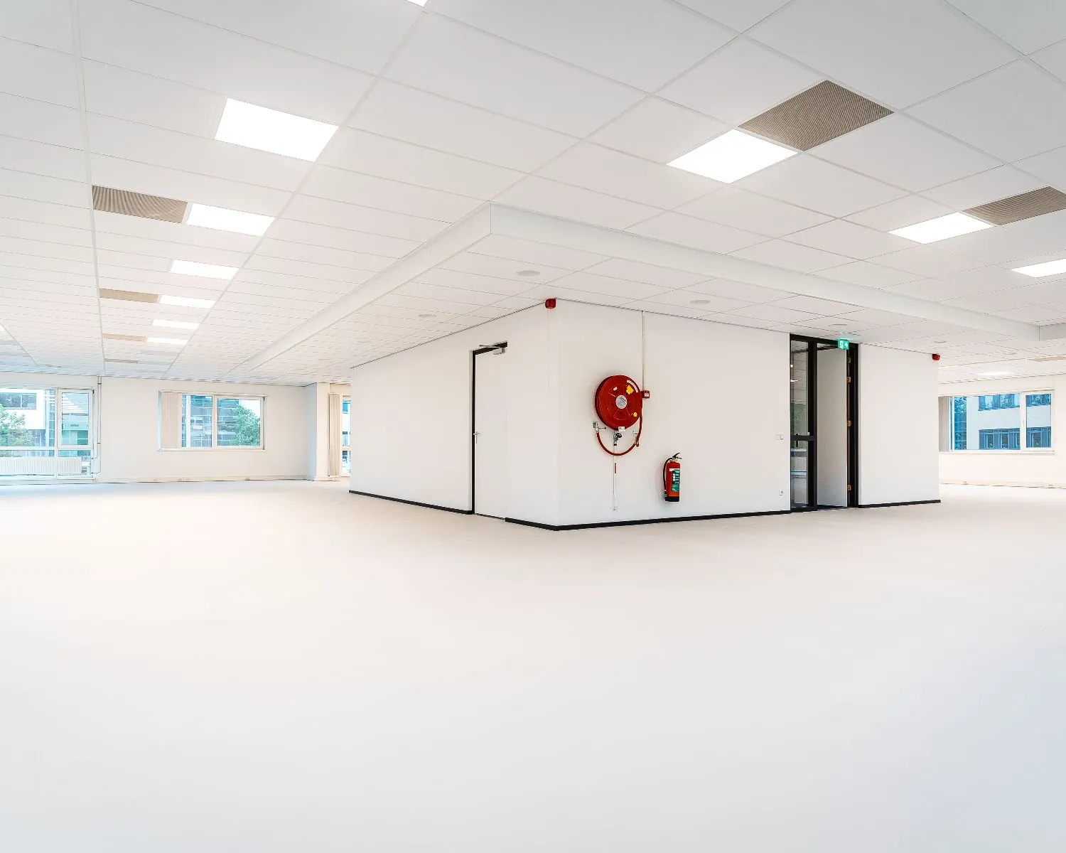 Licht en modern leeg kantoorpand met witte wanden, systeemplafond en grote ramen.