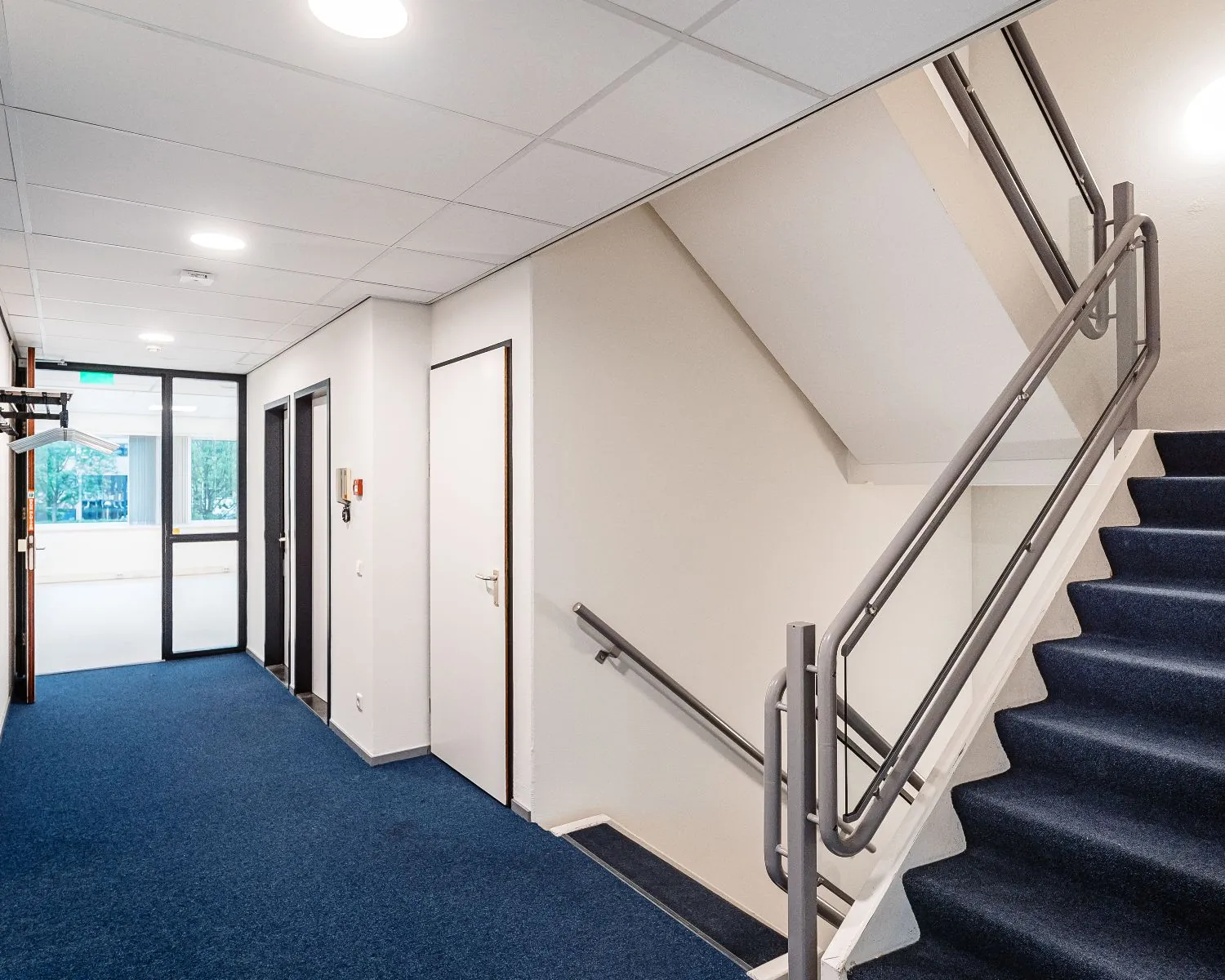 Trapopgang en gang met blauwe vloerbedekking in een kantoorpand van Hanzevast.