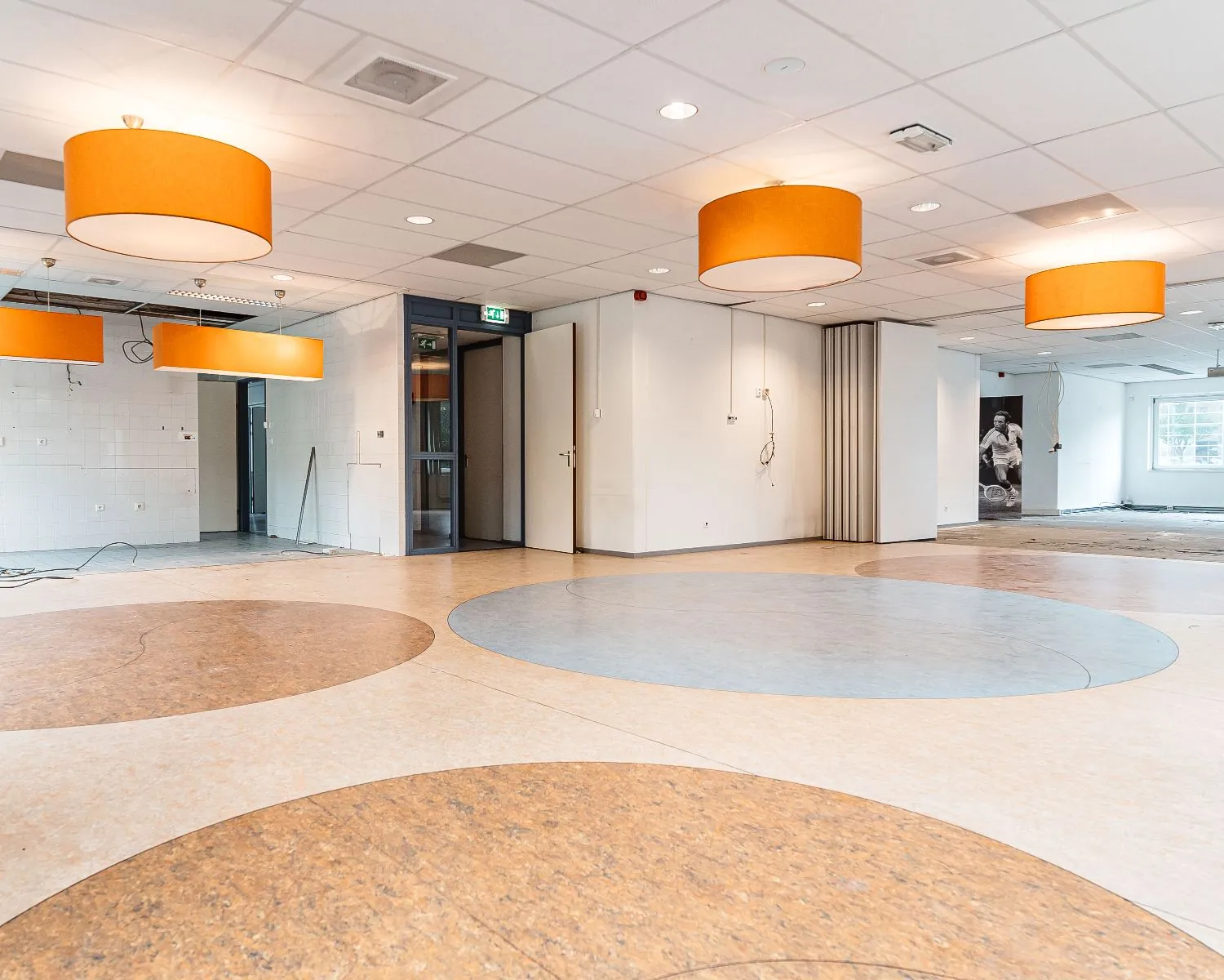 Ruime lege binnenruimte met ronde vloerpatronen en grote oranje plafondlampen, vermoedelijk in een kantoorgebouw van Hanzevast.