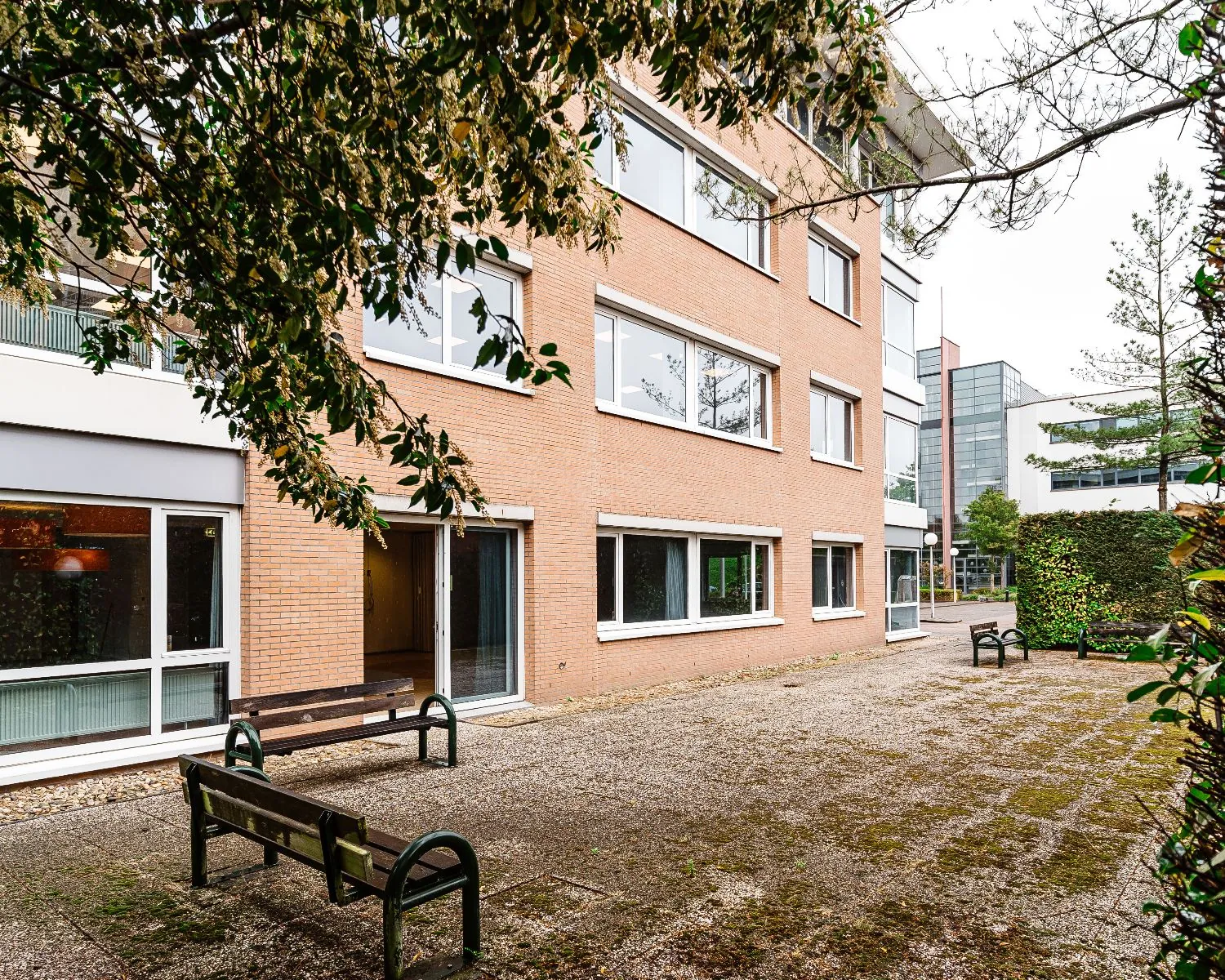 Binnenplein met bankjes naast een modern Hanzevast-kantoorgebouw met bakstenen gevel.