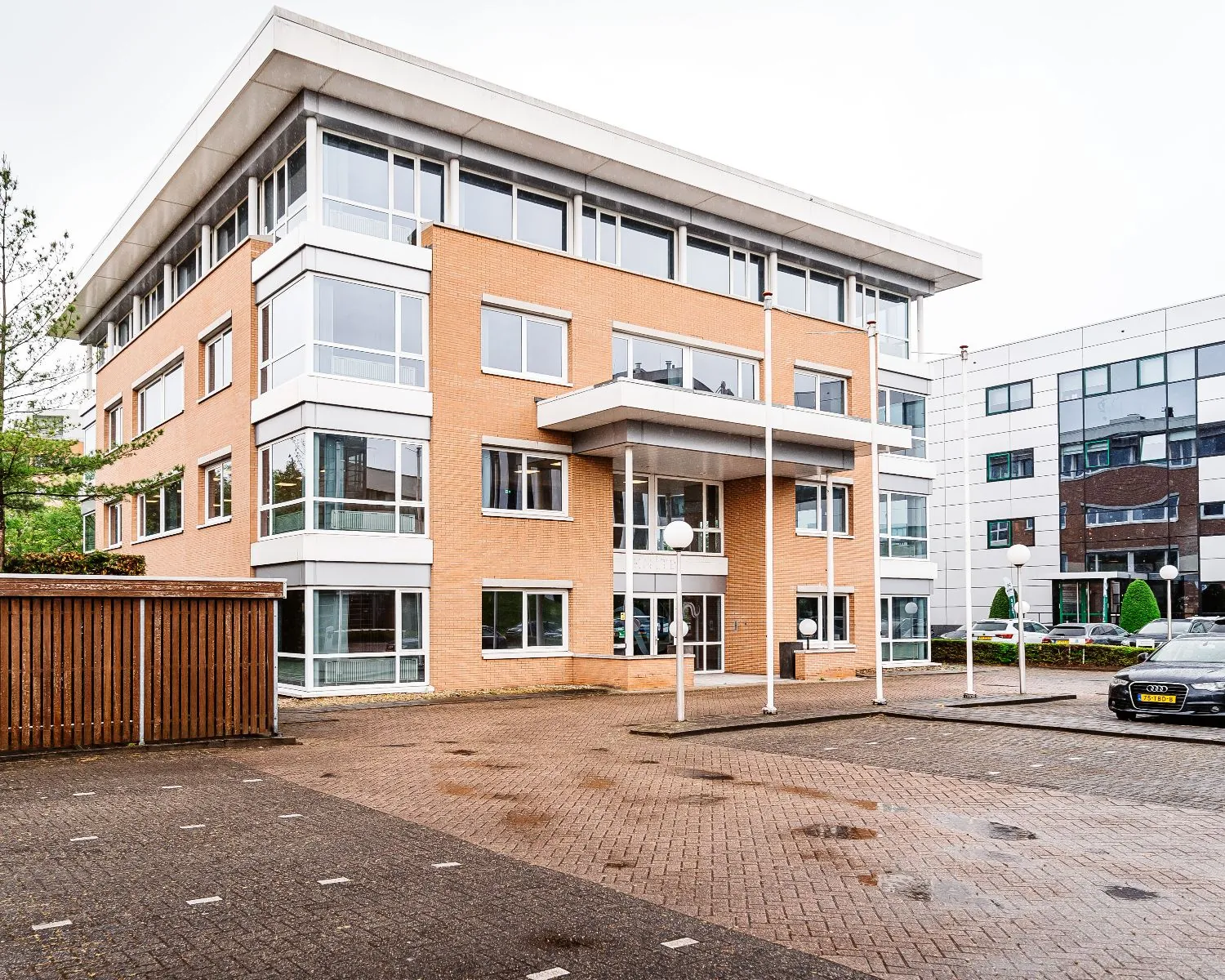 Modern kantoorgebouw van Hanzevast met bakstenen gevel en grote ramen, gezien vanaf de parkeerplaats.