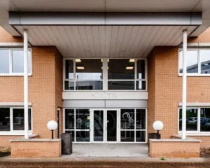 Ingang van een kantoorpand met bakstenen gevel, grote glazen deuren en de naam 'KHTB' boven de entree.