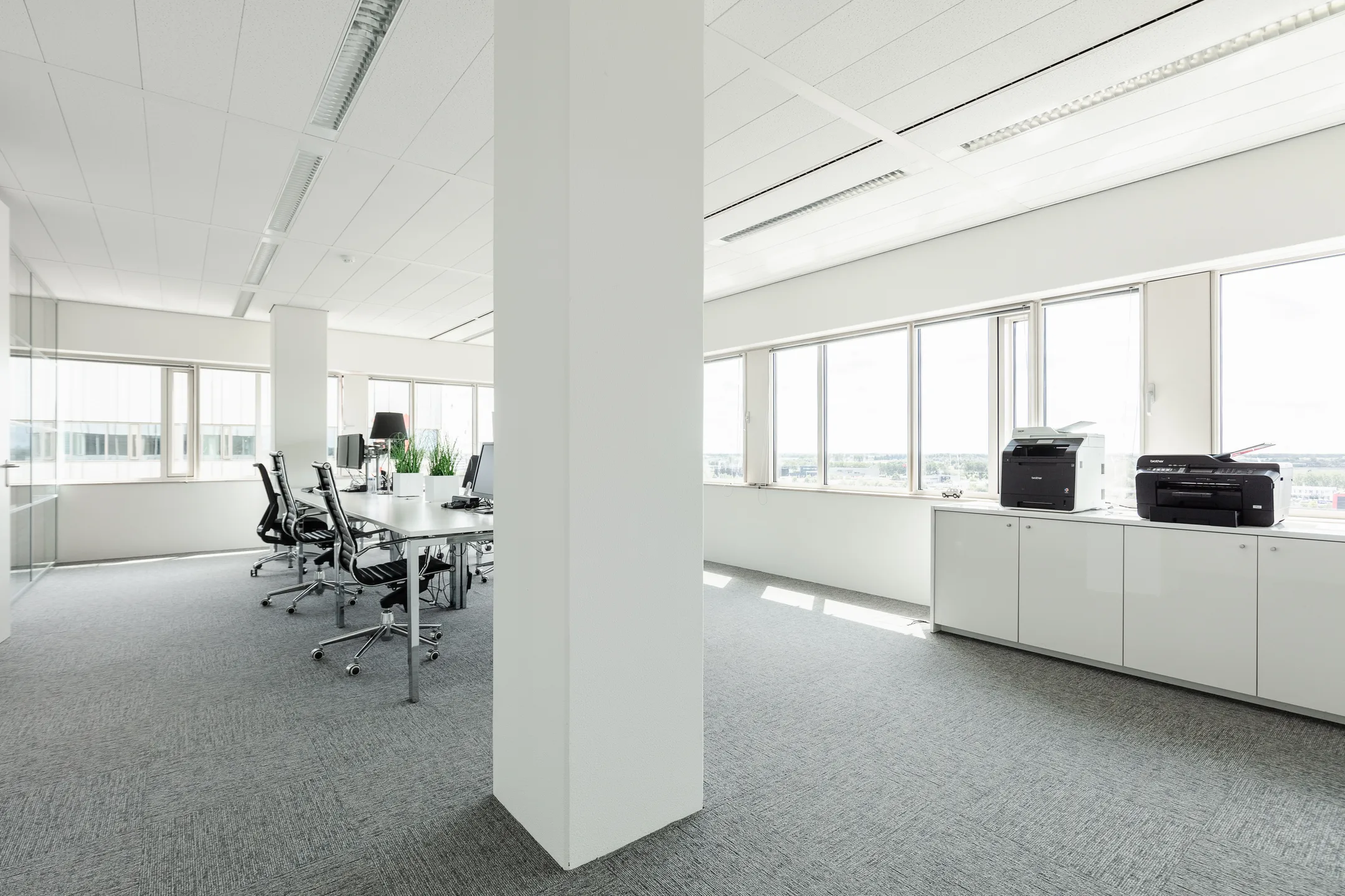 Licht en modern kantoorinterieur aan de Herengracht 204 met werkplekken, bureaustoelen en printers bij het raam.