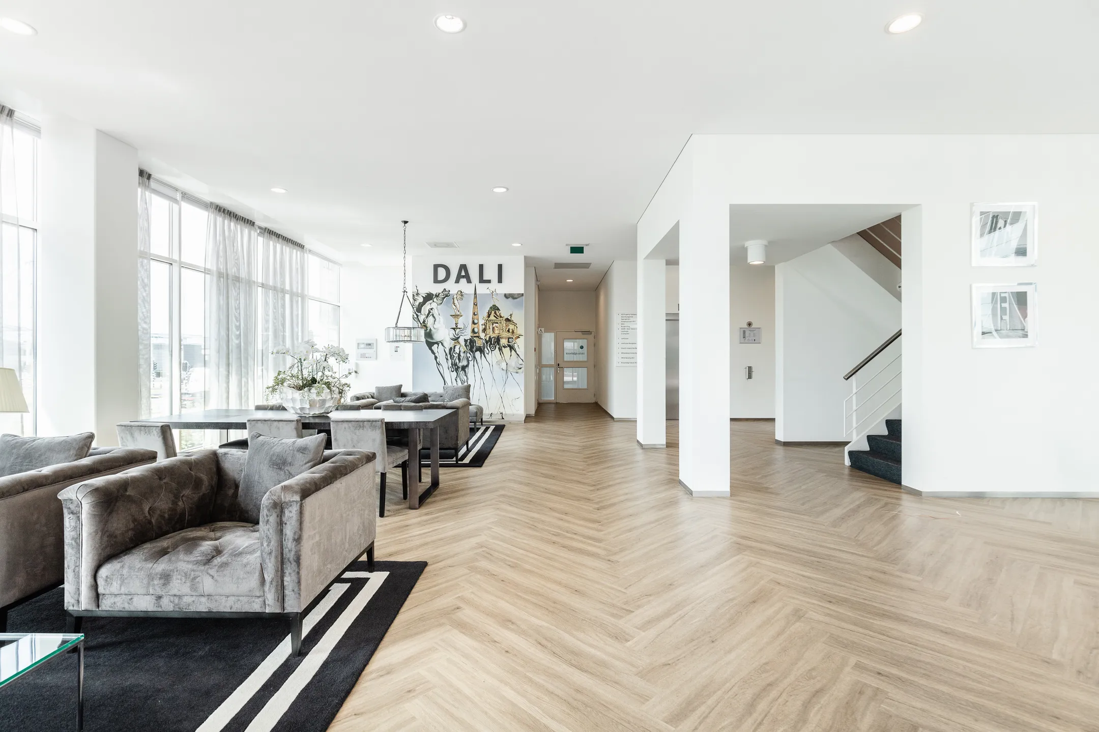 Moderne, lichte lobby met zithoeken, een kunstwerk met de tekst "DALI" en een houten visgraatvloer op Herengracht 204.