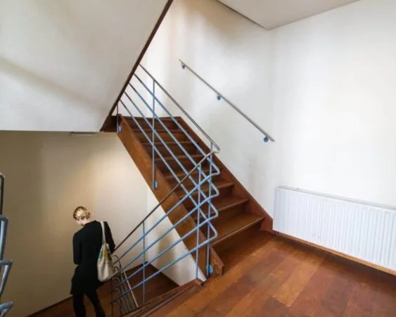 Trap met houten treden en blauw metalen leuning in een licht trappenhuis op Herengracht 211, met een persoon die naar beneden loopt.