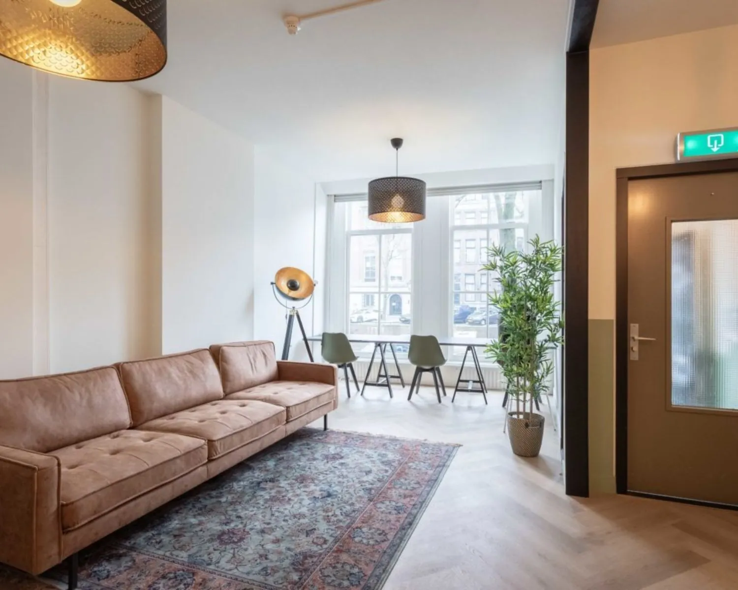 Stijlvolle en lichte zithoek in Herengracht 211 met een leren bank, grote ramen en uitzicht op de gracht.