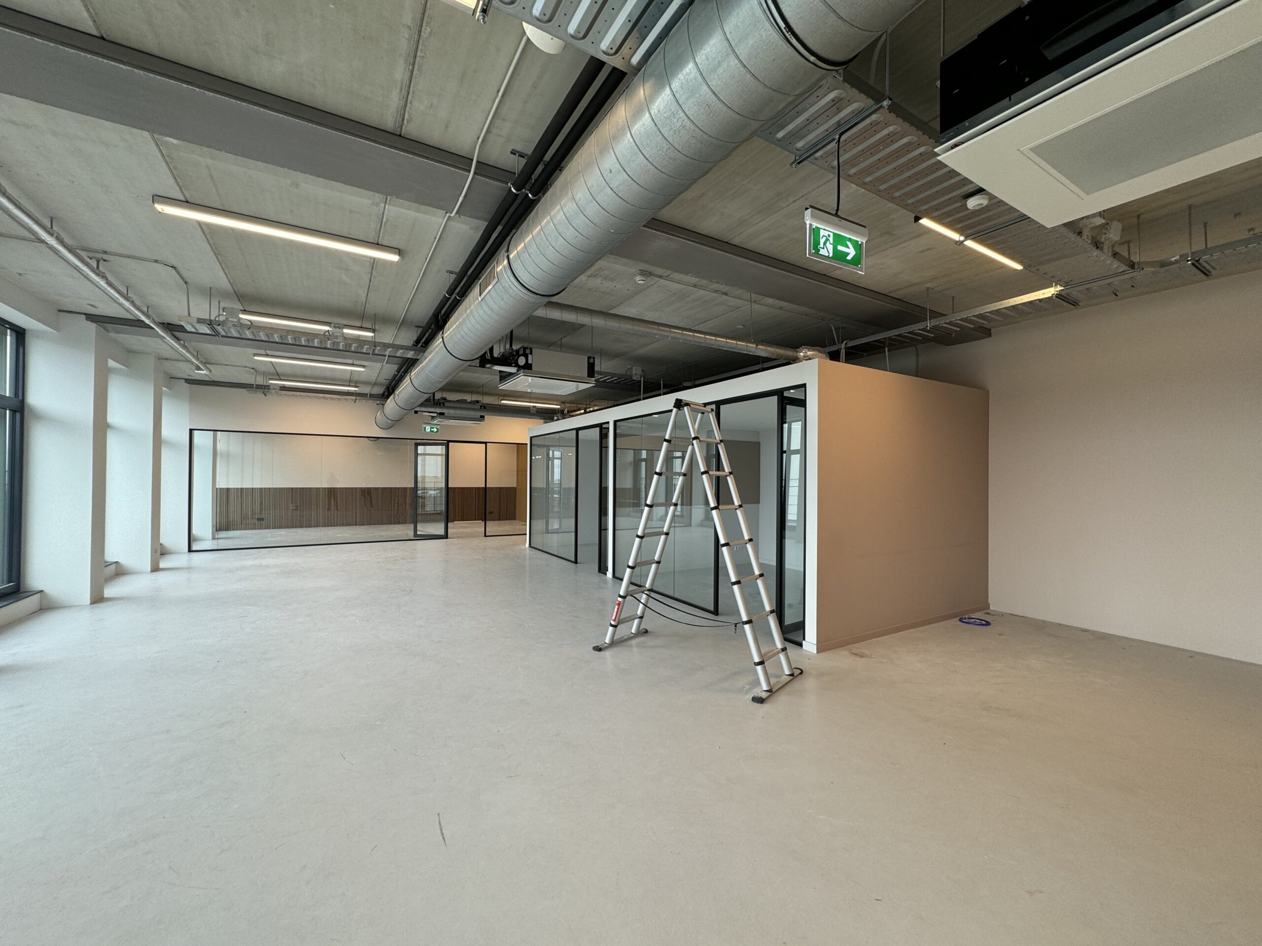 Een leeg, modern kantoorinterieur met een ladder en glazen wanden.