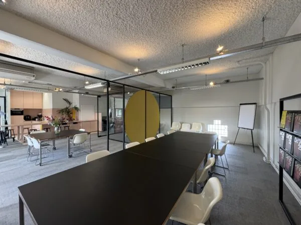 Moderne vergaderruimte met lange zwarte tafel, witte stoelen, flip-over en een open keuken op de achtergrond.