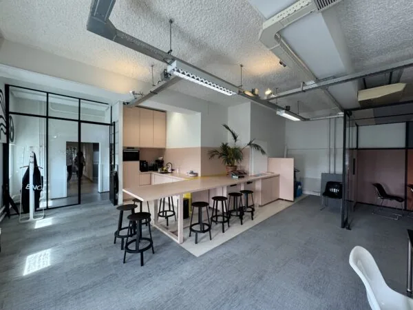 Moderne kantoorruimte met een roze open keuken, hoge tafels met krukken en glazen vergaderruimtes.