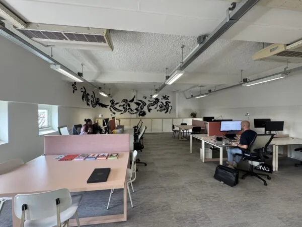 Ruime en moderne kantoorruimte met werkplekken, een muurschildering en enkele mensen aan het werk.