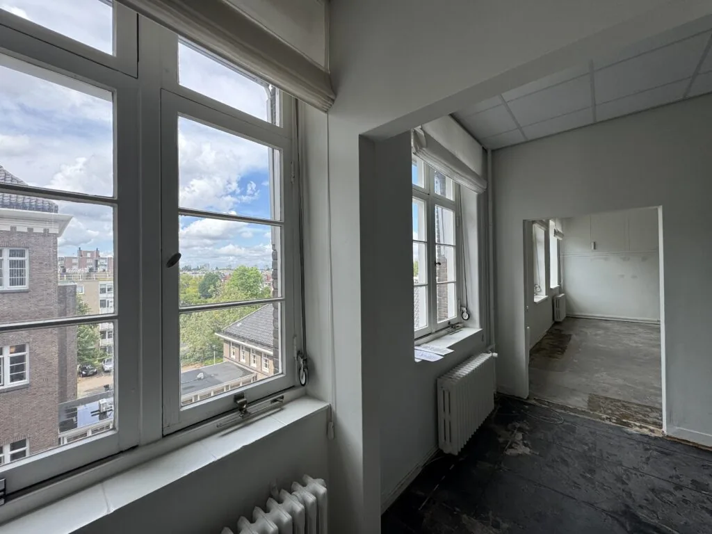 Licht appartement met grote ramen en uitzicht op een stedelijk landschap.