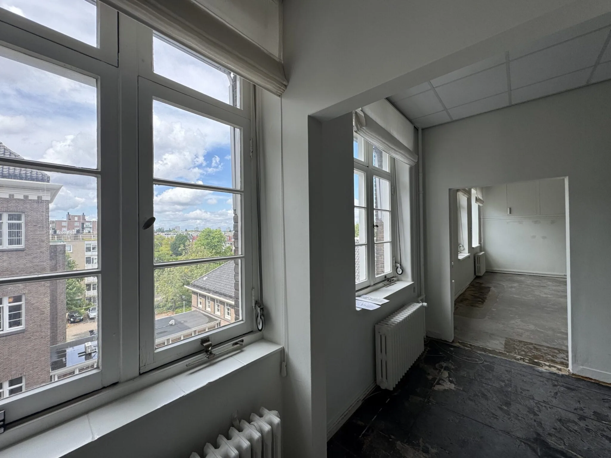 Licht appartement met grote ramen en uitzicht op een stedelijk landschap.