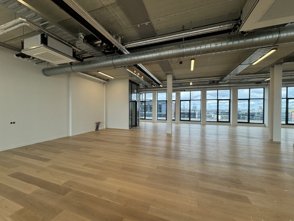 Een ruime, lege kantooretage met houten vloer en grote ramen met uitzicht op de stad.