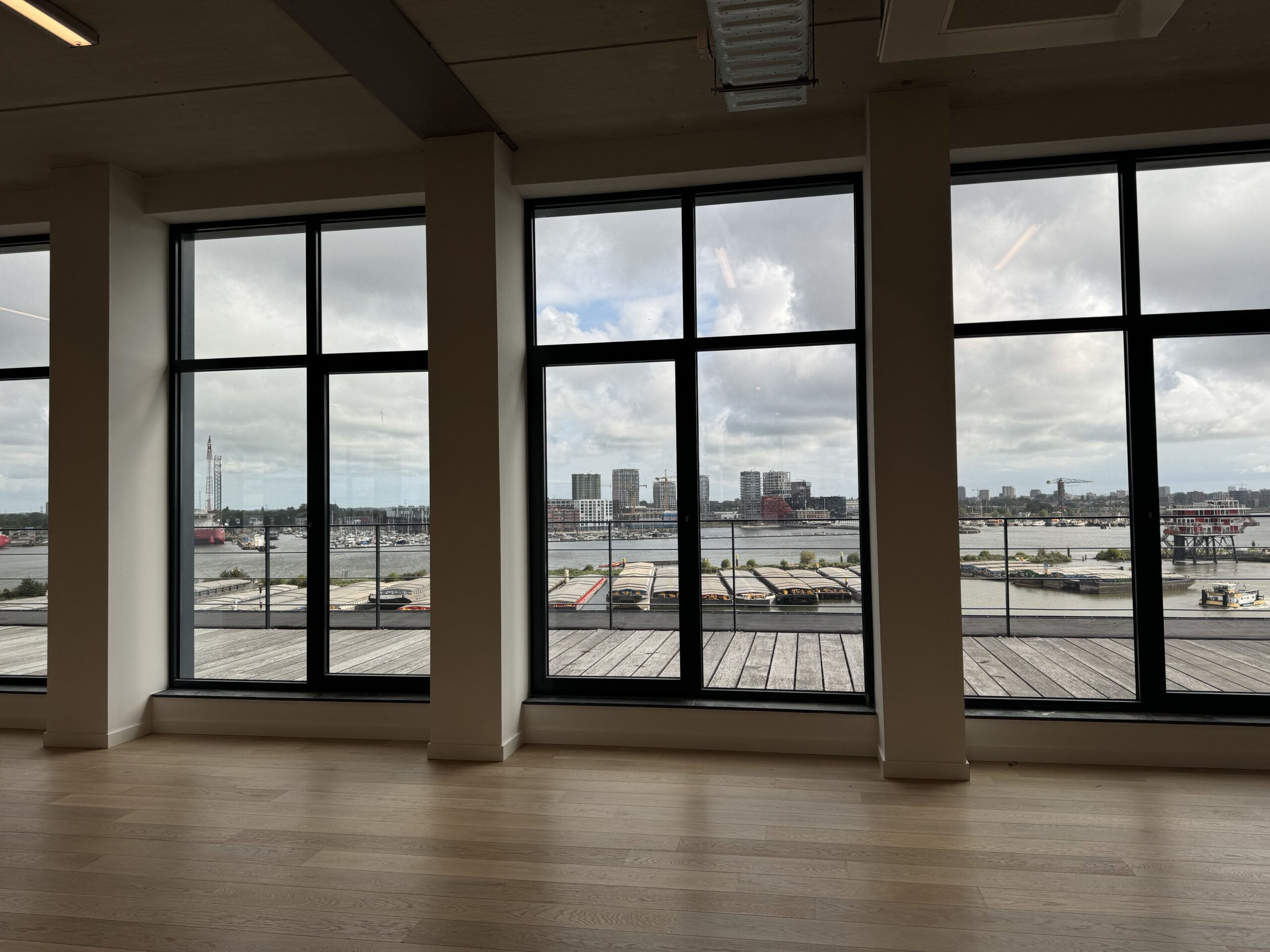 Uitzicht op een haven en stedelijke skyline door grote ramen in een modern gebouw.