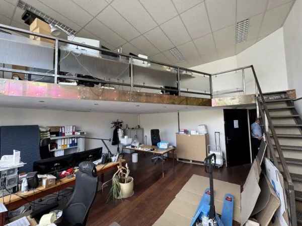 Kantoorruimte met werkplekken, een entresol met extra bureaus en een trap aan de rechterzijde.