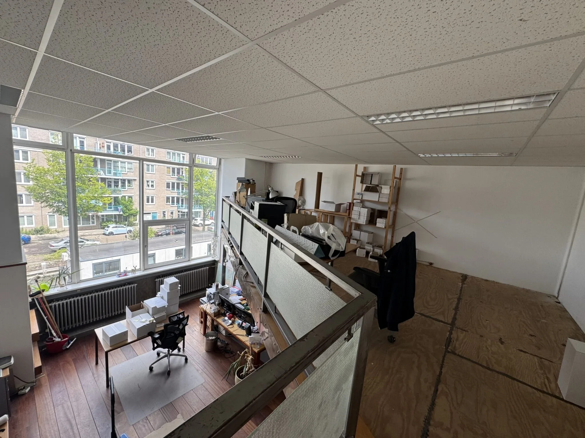 Kantoorruimte met een vide, grote ramen en bureaus met kantoorartikelen en dozen.