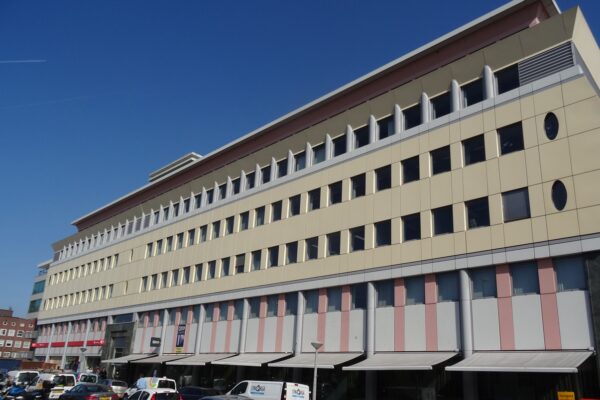 Een modern gebouw met veel ramen en een lichte gevel tegen een heldere blauwe lucht.