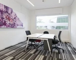 Moderne kantoorruimte te huur Boven de Wolfskuil, met twee bureaus, bureaustoelen, groot raam en kleurrijk bloemenkunstwerk aan de muur.