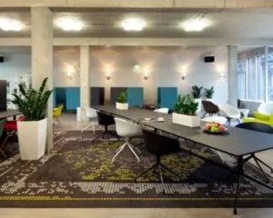 Moderne kantoorruimte aan de Kaldenkerkerweg 20 met strakke inrichting, lange vergadertafels, kleurrijke stoelen en veel natuurlijk licht.