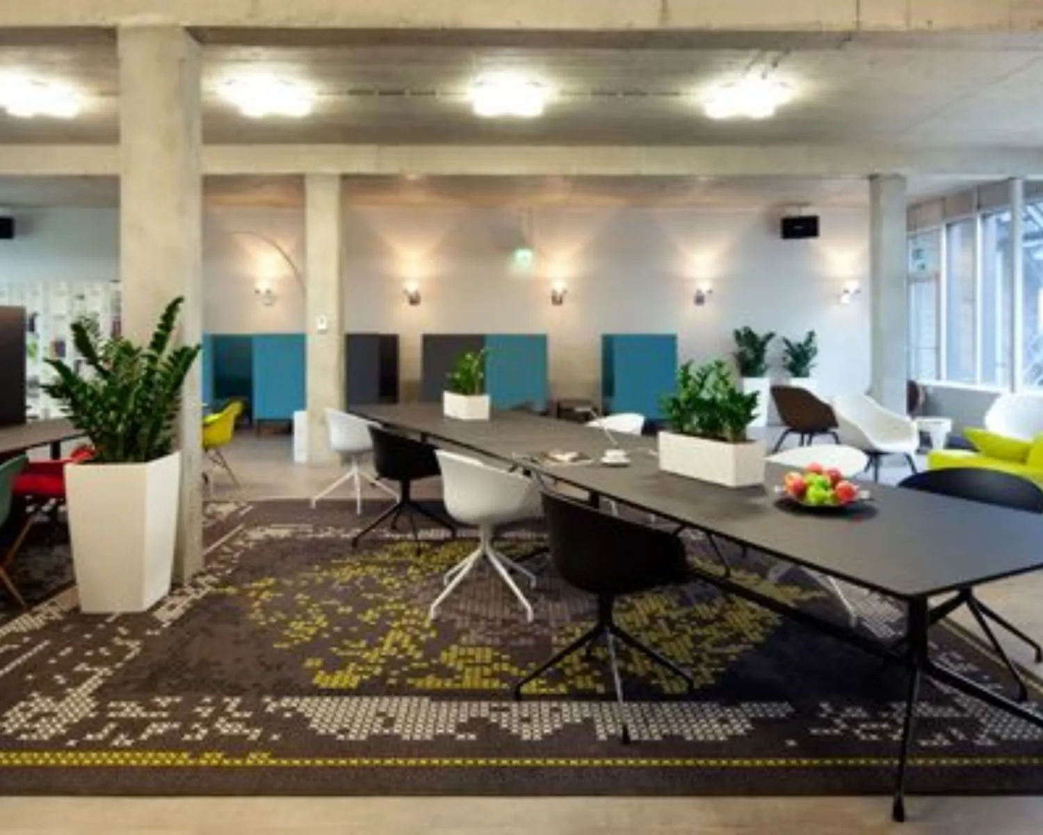 Moderne kantoorruimte aan de Kaldenkerkerweg 20 met strakke inrichting, lange vergadertafels, kleurrijke stoelen en veel natuurlijk licht.