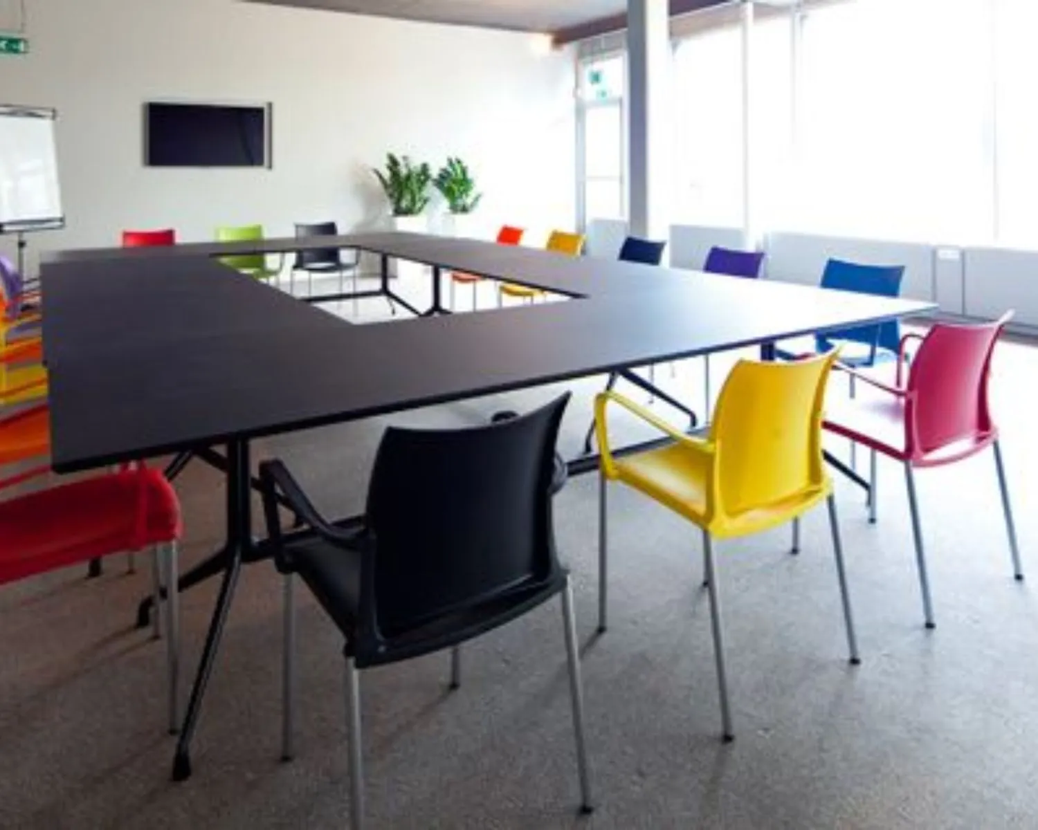 Vergaderruimte met een U-vormige tafel en felgekleurde stoelen aan de Kaldenkerkerweg 20.