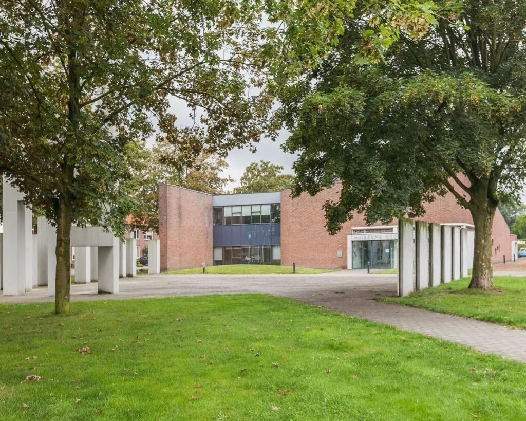 Bakstenen kantoorgebouw aan het Kennedyplein 18 met moderne architectuur, omgeven door bomen en groen.