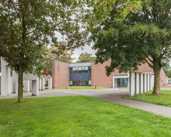 Bakstenen kantoorgebouw aan het Kennedyplein 18 met moderne architectuur, omgeven door bomen en groen.