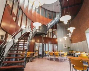 Moderne kantoorruimte aan het Kennedyplein 18 met een open zithoek, gele stoelen en een ronde trap naar de bovenverdieping.