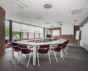 Vergaderruimte met U-vormige opstelling, rode stoelen en grote ramen in kantoorpand aan Kennedyplein 18.